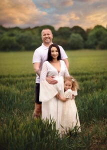 Expecting parents and their young daughter smiling together during a baby bump photo shoot in Nottingham’s countryside.