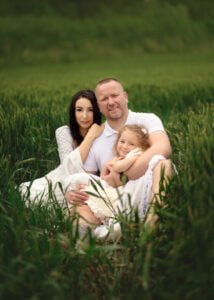 Parents holding their daughter while seated in a field during a baby bump photo shoot in Nottingham.