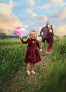 Child holding colorful balloons in the foreground during a baby bump photo shoot in Nottingham’s countryside.
