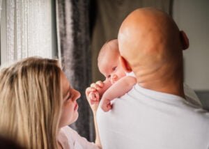 Newborn baby resting on father’s shoulder while the mother watches lovingly during a lifestyle photoshoot in Nottingham.