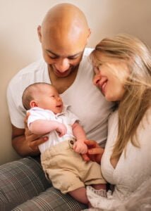 Parents smiling at each other while holding their baby during a relaxed lifestyle newborn photography session at home in Derby.