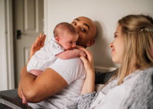 Father holding his baby on his shoulder while the mother smiles during a lifestyle newborn photoshoot.