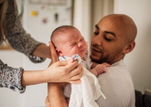 Father wiping his newborn baby’s face during a lifestyle photography session at home in Nottingham.