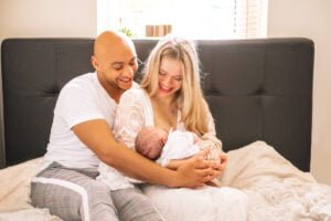 Family sitting on a bed, holding their newborn baby during a natural photography session at home in Nottingham.