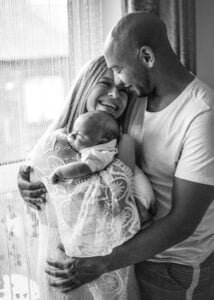 Black and white photo of parents smiling while holding their baby during a lifestyle newborn photoshoot in Nottingham.