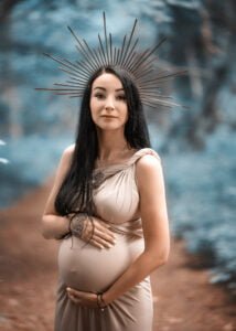 Pregnant woman in a beige gown and golden sunburst headpiece posing for a baby bump photo shoot in Nottingham.