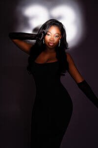 Woman in a sleek black dress posing confidently under a spotlight with “33” shadow during her birthday photoshoot.