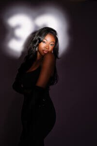 A radiant woman in a chic black dress and elegant gloves celebrates her 33rd birthday with confidence and grace, embodying the spirit of womanhood.