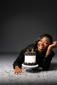 Woman lying on the floor with a “33” birthday cake, surrounded by confetti and laughing joyfully during her photoshoot.