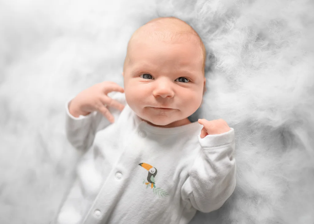 Awake newborn baby lying on a soft white blanket during a newborn photoshoot at home.