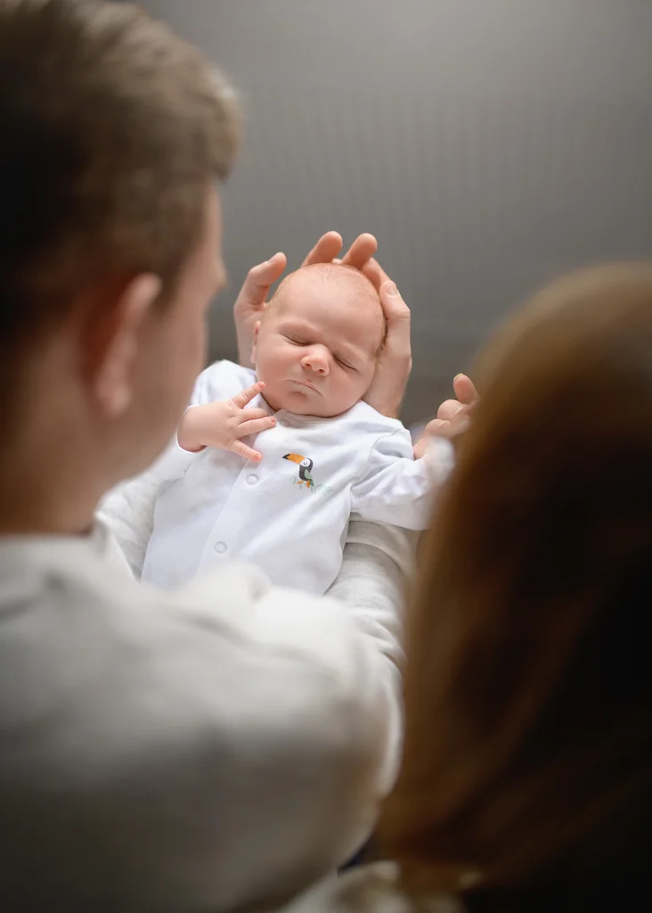 Father gently cradling his newborn baby during a newborn photoshoot at home.