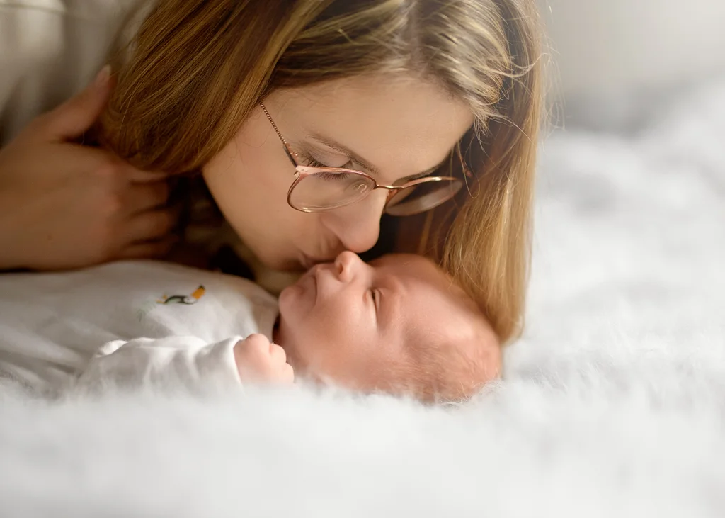Mom tenderly kissing her sleeping baby during a newborn photoshoot at home.