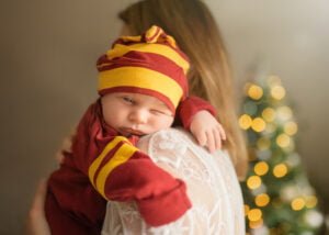 Newborn baby wearing a red hat cuddling on mom’s shoulder during a newborn photoshoot at home.