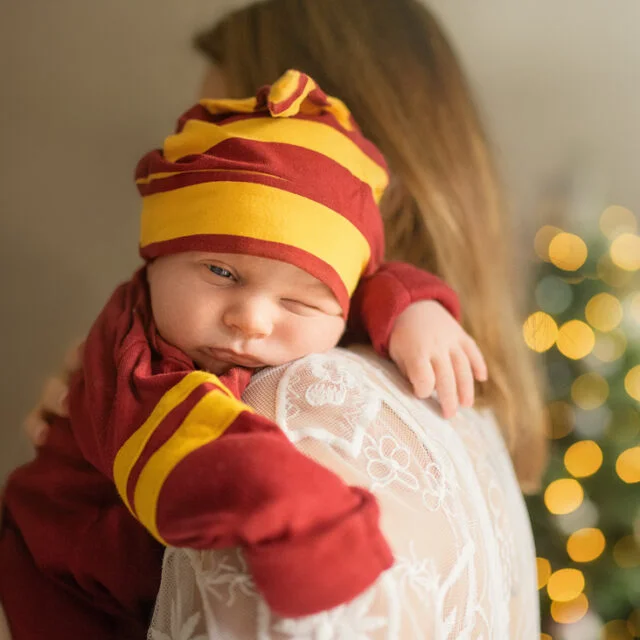 Newborn baby wearing a red hat cuddling on mom’s shoulder during a newborn photoshoot at home.