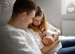 Mom breastfeeding her baby on a bed while dad lovingly watches during a newborn photoshoot at home.