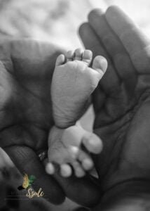 Black-and-white close-up of a newborn’s tiny feet cradled in parents' hands during a newborn photoshoot at home.