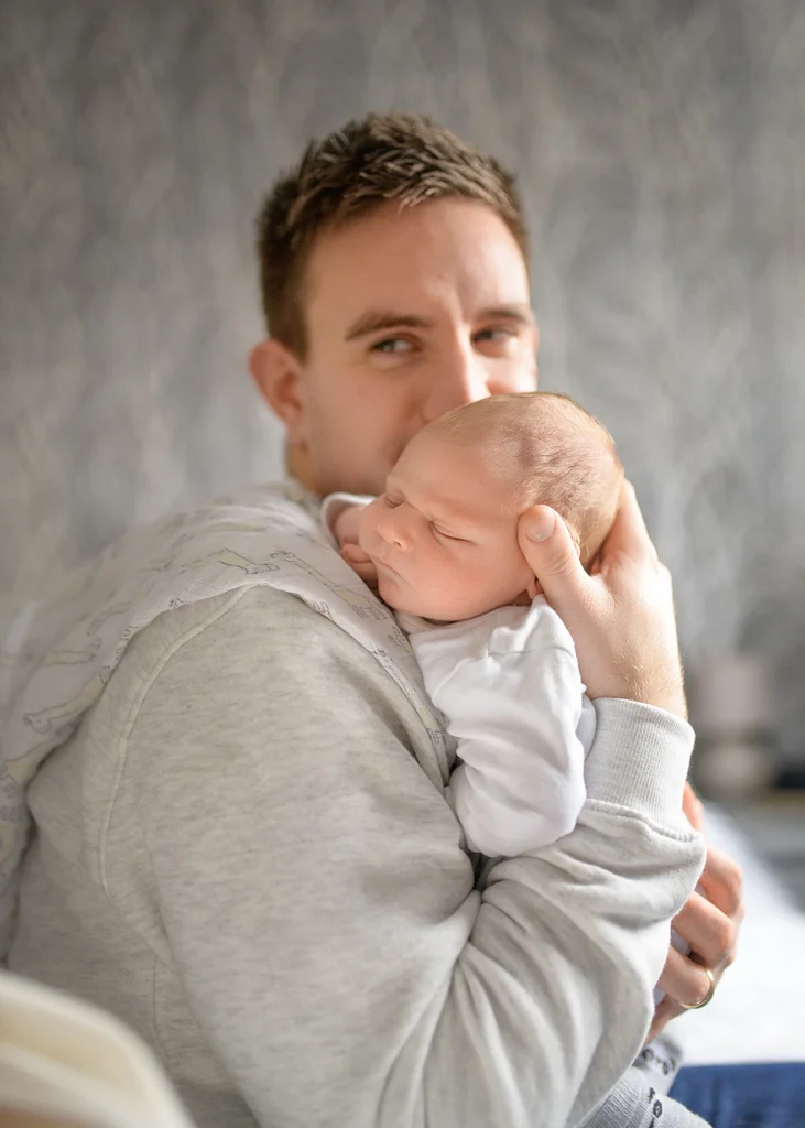 Father holding his newborn baby over his shoulder in a cozy setting during a newborn photoshoot at home.