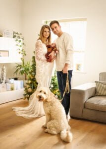 Family with their newborn baby and dog standing by a decorated Christmas tree during a newborn photoshoot at home.