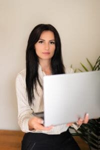 Female professional holding a laptop and looking confident during a professional business photoshoot, ideal for branding and corporate profiles.