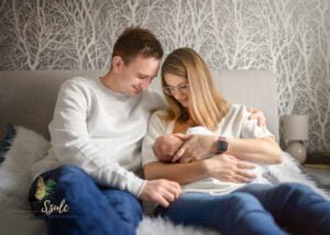 Parents sitting on a bed holding their newborn baby lovingly during a newborn photoshoot at home.