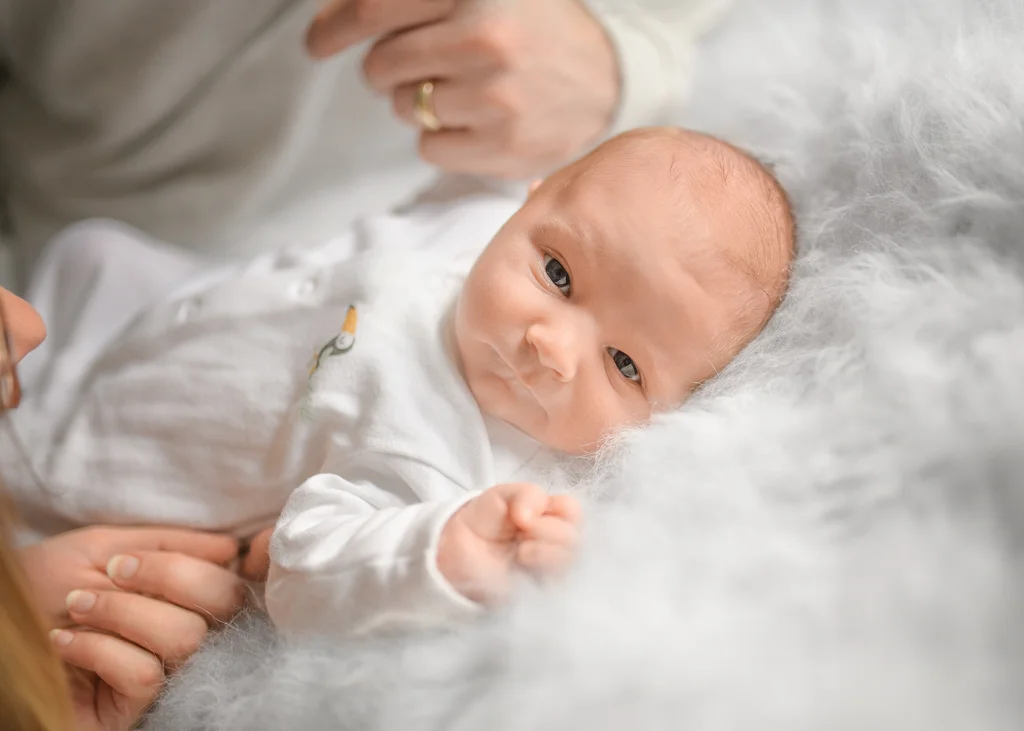A newborn baby lying awake on a soft fluffy blanket during a newborn photoshoot at home.