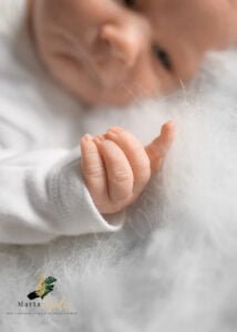 Close-up of a newborn baby’s tiny hand resting on a soft white blanket during a newborn photoshoot at home.