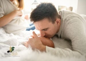 Dad kissing his newborn baby on a fluffy blanket during a cozy newborn photoshoot at home.