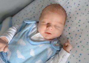 A peaceful newborn baby sleeping in a blue outfit with cloud patterns during a newborn photoshoot at home.