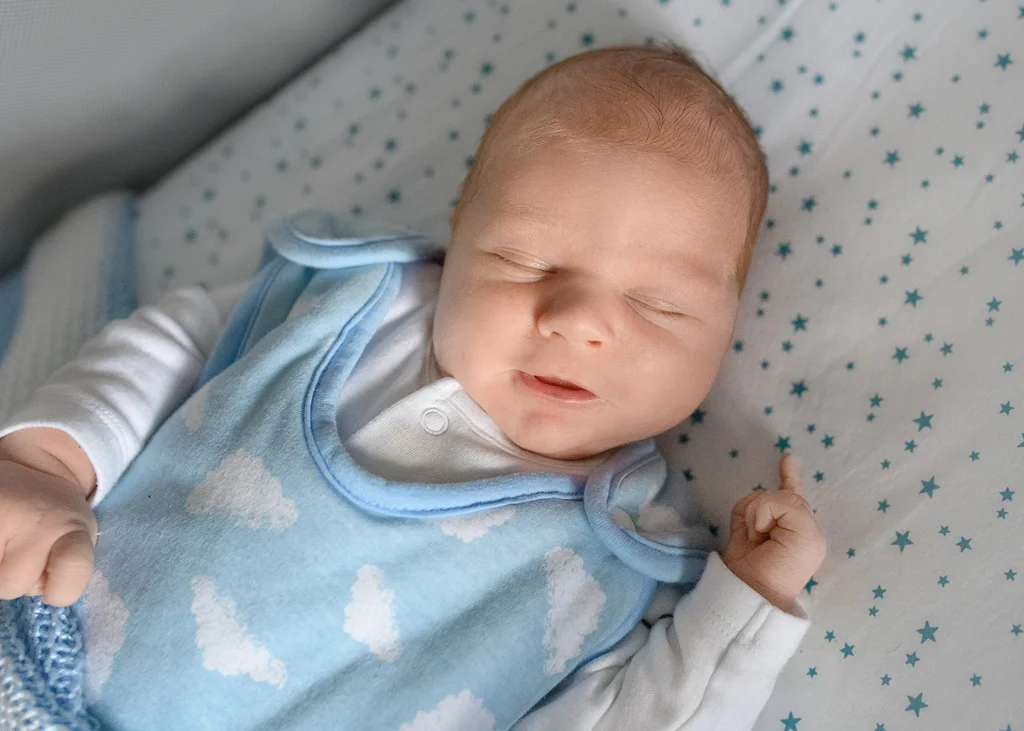 A peaceful newborn baby sleeping in a blue outfit with cloud patterns during a newborn photoshoot at home.