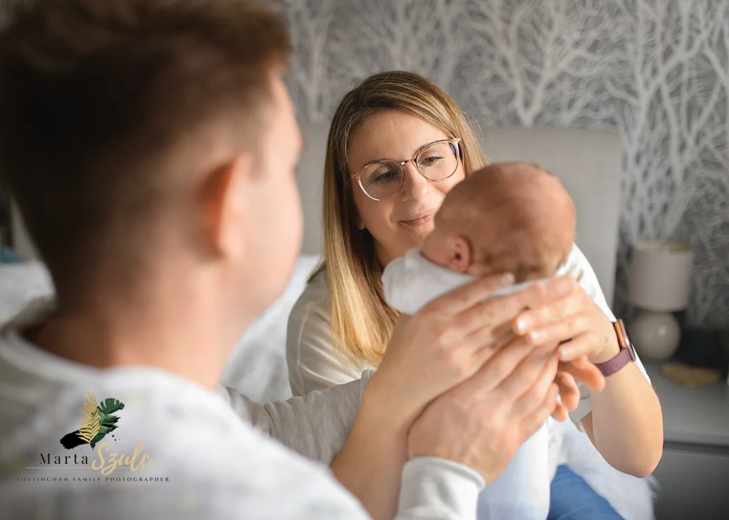 Parents lovingly admiring their newborn baby while holding them during a newborn photoshoot at home.