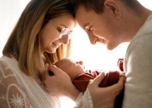 Parents holding their newborn baby together in soft natural light during a newborn photoshoot at home.