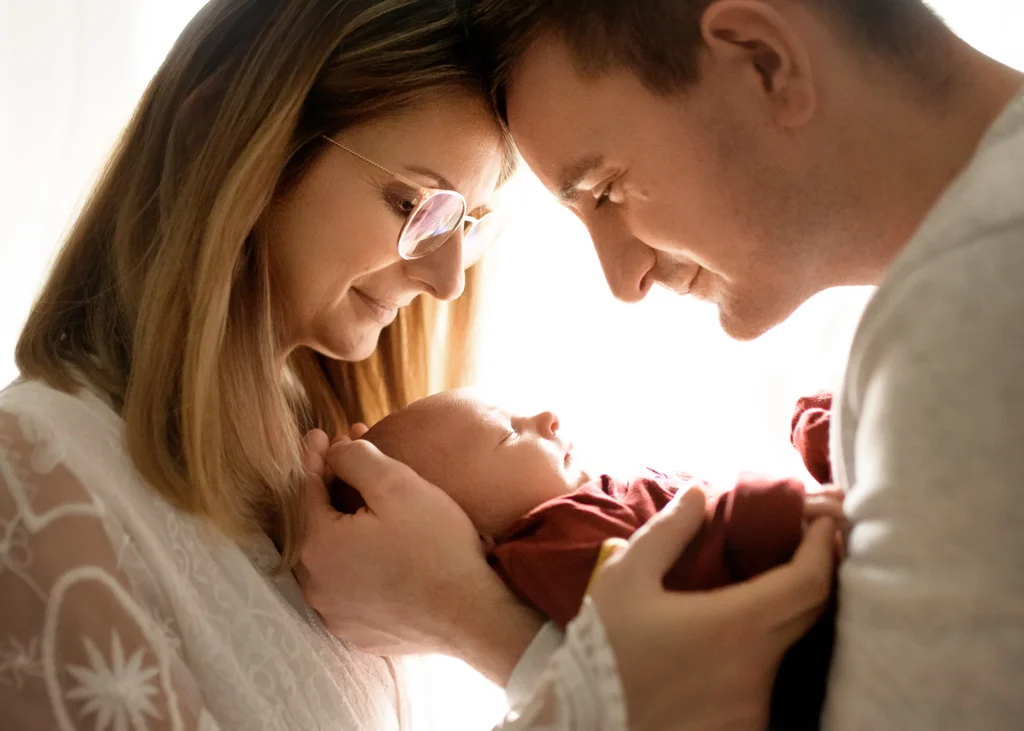 Parents holding their newborn baby together in soft natural light during a newborn photoshoot at home.