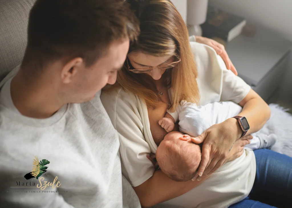 Mom breastfeeding newborn baby while dad lovingly watches during a newborn photoshoot at home.