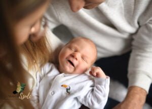 A smiling newborn baby being held by their parents during a newborn photoshoot at home.