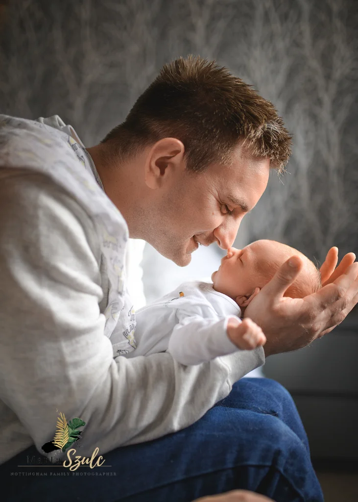 Father smiling and touching noses with his newborn baby during a heartfelt newborn photoshoot at home.