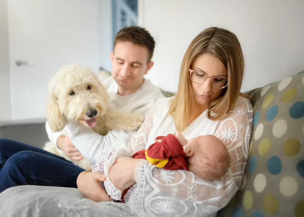Family sitting on a couch with their newborn baby and family pet during a newborn photoshoot at home.