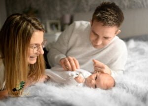 Parents smiling and playing with their newborn on a master bed during a newborn photoshoot at home.