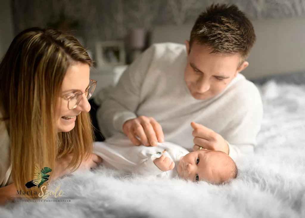 Parents smiling and playing with their newborn on a master bed during a newborn photoshoot at home.