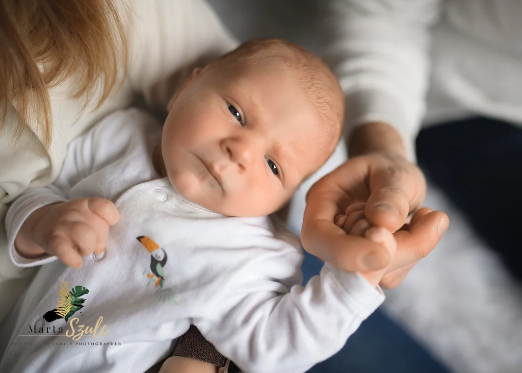 Newborn baby holding mom’s finger while relaxing on her lap during a newborn photoshoot at home.