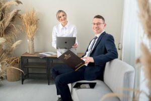 Male and female professionals during a professional business photoshoot, sitting with a laptop and documents in a stylish office setting.