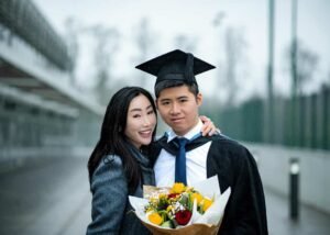 Joyful couple celebrating graduation at the University of Nottingham, sharing a moment in the rain with a bouquet of flowers.