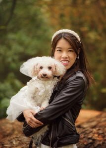 Bride holding her dog dressed in bridal attire during a pre-wedding photoshoot in a woodland setting.