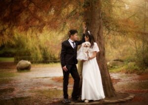 Couple leaning against a tree with their dog during a pre-wedding photoshoot at Elvaston Castle in a rustic autumn setting.