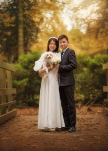 Couple standing on a bridge during their pre-wedding photoshoot at Elvaston Castle, holding their dog and flowers.