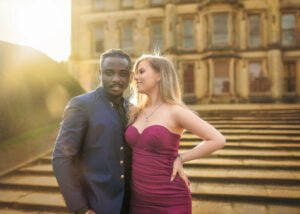 Engaged couple posing in front of a historic building during their engagement photoshoot at sunset.