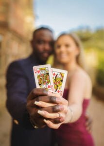 Engaged couple holding playing cards depicting the King and Queen of Hearts during their engagement photoshoot.