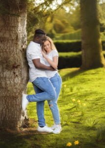 Couple sharing an intimate embrace under a tree during their engagement photoshoot in a sunlit park.