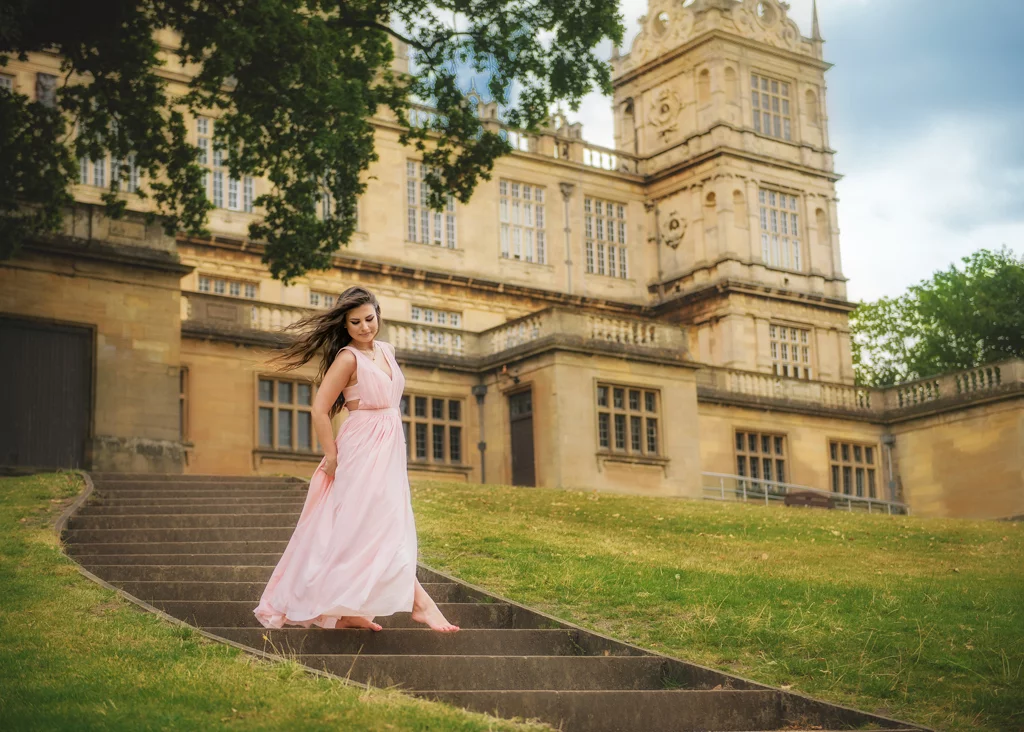 Outdoor female portrait photography of a woman in a pink dress walking down the stairs of a historic building