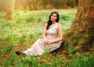 A mother in an elegant dress sitting by a tree surrounded by daffodils during a Mother and Child Photoshoot in Nottingham.
