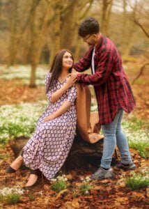 A smiling couple enjoying a playful moment near a tree during their outdoor photoshoot for women in a woodland location.